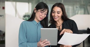 Birlikte tabletten online proje içeriğini izleyen, arayüz, yazılım ürünü için çözümü tartışan, dijital aleti takım çalışması için kullanan, gülümseyen çok ırklı kadın iş arkadaşları.