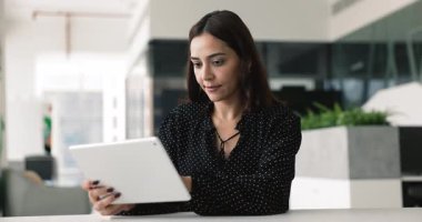 Ofiste tablet bilgisayar kullanan güzel bir Orta Doğulu iş kadını, online iş içeriğine göz atıyor, profesyonel web servisini iş için kullanıyor, internete ve nöral ağa danışıyor.