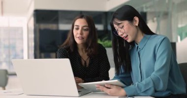 İki genç çok ırklı ürün yöneticisi iş yerinde aygıtlar kullanıyor, tablet ve dizüstü bilgisayardaki pazarlama istatistiklerini karşılaştırıyor, çevrimiçi içeriği analiz ediyor, rapor ediyor, İnternet satışlarını tartışıyorlar.