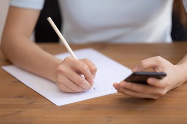 Bin yıllık kız el yazısını kağıda kapat cep telefonu kablosuz internet arama bilgisini kullan, kız öğrenci notlar yaz mesaj ya da sınav için hazırlan, akıllı telefon web sitesine bak