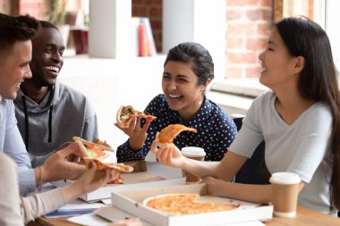 Heyecanlı çeşitli bin yıllık öğrenciler yemek molasında servis edilen lezzetli pizzanın tadını çıkarırken kahkahalar ve şakalar yapıyorlar. Aşırı neşeli çoklu etnik kökenli gençler lezzetli İtalyan fast food yiyor.