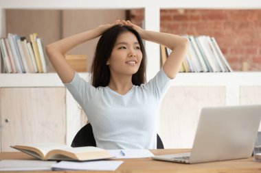 Milenyum güzeli etnik kız masa başına oturur uzaktan düşünür ya da görselleştirir düşüncelere dalmış Asyalı kız öğrenci iş yerinde rüya görmeyi öğrenmekten alıkoyar.