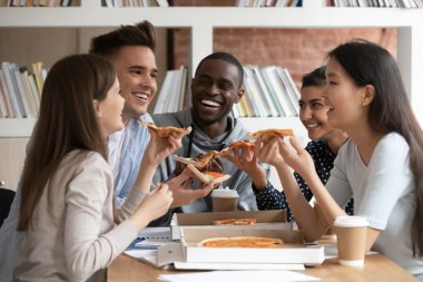 Mutlu çoklu etnik gruptan gençler masada oturup öğle yemeğinde İtalyan fast food 'u yerken eğleniyorlar. Çok ırklı öğrenci grupları yemek molasından sonra lezzetli pizzaların tadını çıkarıyorlar.