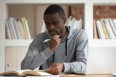 Düşünceli Afro-Amerikan milenyum adamı masada oturmuş ders kitabı okumakla meşgul. Düşünceli, çift ırklı erkek öğrenci kitaplarla çalışıyor. Sınava ya da sınava hazırlanıyor.
