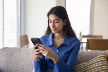 Düşünceli Hintli kadın akıllı telefonunu evde kullanıyor, kanepede tek başına oturuyor cihaz ekranına bakıyor, organizatörü, planlayıcıyı, mesajı kontrol ediyor, bildiriyi okuyor, cevap üzerinde kafa yoruyor, internette vakit geçiriyor.