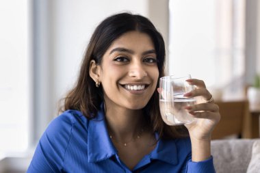Kapalı portre genç gülümseyen güzel Hintli kadın elinde bir bardak maden suyu tutuyor, pozitif ve rahat görünüyor, serinletici içkinin tadını çıkarıyor, hidrasyon ve refahı teşvik ediyor, sağlıklı yaşam tarzını koruyor.