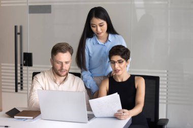 İşbirlikçi iş. Genç kadın liderli üç farklı etnik gruptan oluşan iş dünyası ekibi, iş yerindeki not defterini kullanarak finansal raporları analiz eden belge metinleri geliştiriyor.