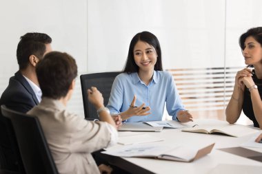Etkileşimli tartışma. Mutlu gülümseyen Asyalı kadın takım lideri proje yöneticisi çeşitli çok ırklı şirket ekibiyle brifing hakkında açık bir diyalog kurup görüşlerini sor fikir önerilerini dinle.