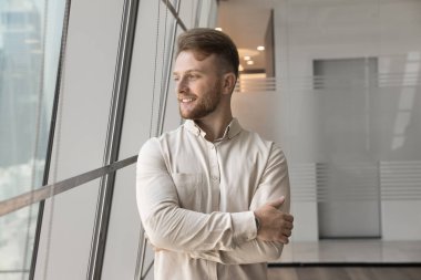 Genç ve hırslı. Neşeli, kendine güvenen bin yıllık iş adamı çalışanı ofis penceresinin yanında durmuş, meslekte başarılı bir gelecek için iş vizyonuna odaklanmış şehir manzarasına bakıyor. Boşluğu kopyala.