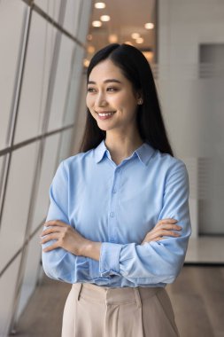 Başarı ve güven. Güzel Asyalı genç bayan öğrenci bürosu çalışanı modern ofiste kollarını kavuşturup uzaktan bakan iş kadını kariyer hedeflerini yansıtıyor yenilikçi fikirler yaratıyor.