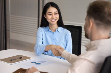 Yetenek kiralamak. Mutlu gülümseyen genç Asyalı kadın iş başvurusu erkek İK yöneticisiyle el sıkışıyor. İş projesi fikri sunulduktan sonra profesyonel iş görüşmesi için işe alınıyor.