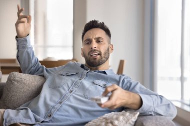 Sinirli yüz ifadesiyle TV izleyen bir adam, sık sık yaptığı reklamlar yüzünden kızgın, kendisini rahatsız eden çok sayıda reklamdan rahatsız, ilginç olmayan içerik, teknik sorunlar veya kaçırılan programlardan.