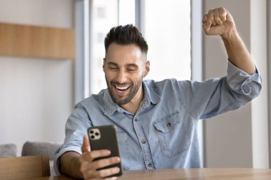 Heyecanlı adam akıllı telefona bakıyor, bağırıyor, harika haberleri kutluyor, favori takım maç ya da turnuva kazandı, hedefe ulaşılması hakkında bilgilendirme veya mesaj aldı, yarışmayı kazandı, hediye verdi, ya da piyango kazandı.
