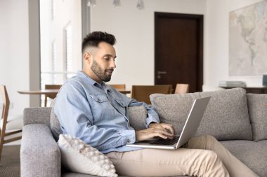 Yakışıklı İspanyol adam, ticari pazar platformu üzerinden modern dizüstü bilgisayar, mal ve elektronik hizmetler satın almak veya sipariş etmek, İnternet üzerinden çalışmak ve uzaktan eğitim görmek suretiyle boş zamanını evde geçiriyor.