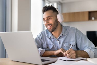 Çevrimiçi çalışan gülümseyen adam, internete bağlı kablosuz kulaklık takan, yeni profesyonel bilgiler edinen, ses kurslarını dinleyen, yabancı dil becerileri geliştiren. Modern teknolojiyi kullanan eğitim