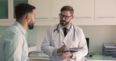 Ciddi bir doktor hastaya sağlık şikayetleri, hastalık belirtileri, doldurma kayıtları, anket, başvuru, tıbbi geçmiş belgelerinde klinikteki randevuyla ilgili notlar soruyor.