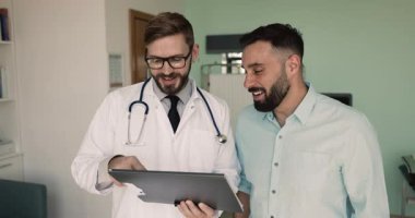 Mutlu erkek doktor, sağlık raporunu olumlu hastaya açıklıyor. Kağıt üzerinde iyi haberler gösteriyor. Muayeneden sonra iyimser haberler veriyor.