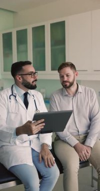 Ciddi bir erkek doktor klinikteki kanepede hastayla konuşuyor, sağlık kontrolü sonuçlarını anlatıyor, belge gösteriyor, muayene kağıtlarını analiz ediyor, erkeklere danışmanlık yapıyor.