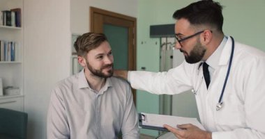 Pozitif doktor erkek hastaya iyimser haberler veriyor, sağlık raporunu, muayene sonuçlarını, omuza destekle dokunmayı, başarılı bir tedaviden sonra iyileşme için teşvik etmeyi anlatıyor.