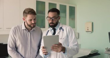 Kendine güvenen genç Latin doktor muayene sonuçlarını gösteriyor, tabletle pozitif hastaya tarama yapıyor, sağlık raporunu açıklıyor. Alet kullanarak, konuşarak, gülümseyerek.