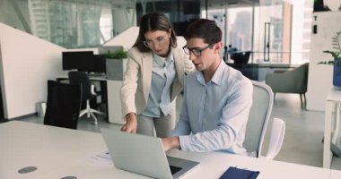 Genç Latin profesyonel kadın iş arkadaşına tavsiye veriyor, monitörü işaret ediyor, konuşuyor. Şirket çalışanları ve yöneticileri birlikte bilgisayar projesinde çalışıyorlar.