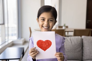 Şirin Hintli sanatçı kızın portresi oturma odasında kırmızı kalpli kartpostal göstererek anne ya da babaya içten bir mesaj hazırlıyor. Hayat olayları, tatiller, hobiler.