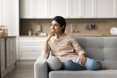 Hoş düşünceler. Rahat, düşünceli genç bayan modern ev stüdyosunun rahat kanepesinde oturmaktan hoşlanıyor. Uzağa bak. İç dizayn değişikliklerinin emlak sigortası planladığını düşün. Boşluğu kopyala