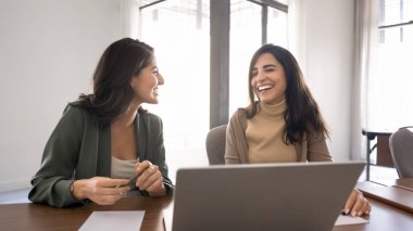 Olumlu sohbete katılan iki kadın meslektaşı şirket ofisinde dizüstü bilgisayar, kahkaha, ortak görev, proje tamamlama veya işle ilgili konularla bir araya geldiler. Bölüm işbirliği, takım çalışması