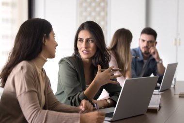 Kadın, masa başında dizüstü bilgisayarla oturan, beyin fırtınası veya karar verme sürecine katılan, birlikte çalışma ofisindeki toplantı sırasında yapılacak iş ve hedefler için stratejileri tartışan bir meslektaşa fikrini açıklar veya sunar.