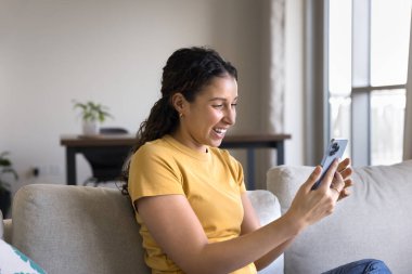 Genç kız akıllı telefonuyla kanepede oturuyor, sosyal medya ağlarında komik videolar izliyor, içeriğe gülüyor, boş zamanlarını internette geçiriyor. Modern teknoloji aşırı kullanımı, yeni mobil uygulama kullanımı