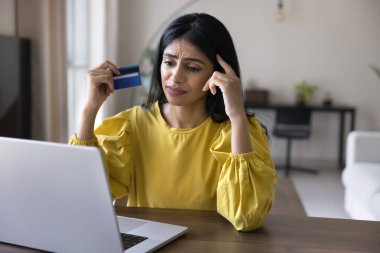 Üzgün Hintli bir kadın dizüstü bilgisayar kartına bakar, satın almaya çalışır, ödeme ile ilgili sorunlar yaşar veya yetersiz fonlar, beklenmedik suçlamalar, dolandırıcılık endişeleri yüzünden işlem yapmayı reddeder.