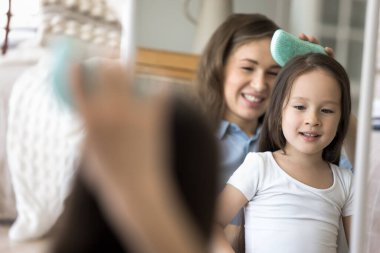 Aşk günlük ritüele yansıyor. Ayna yansıması sevgi dolu genç anne kucağında sevimli küçük bir kız kucağında kızının uzun saçlarını plastik masaj fırçasıyla dikkatlice tarıyor. Boşluğu kopyala