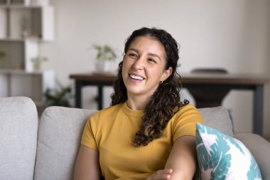 Kahverengi kıvırcık saçlı, gülen genç Brezilyalı kadın rahat bir şekilde koltukta oturuyor, kıkırdıyor, hoş sohbetlerden keyif alıyor ya da mutlu anılarını hatırlıyor. Pozitif ruh hali, iyimserlik, rahatlık.