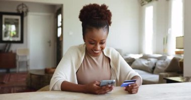 Mutlu Afrikalı genç Amerikalı banka müşterisi evde akıllı telefon ve kredi kartı kullanıyor, iyi sürpriz haberler alıyor, ödülü kazanıyor, başarıyı kutluyor, zafer, zafer, kahkaha