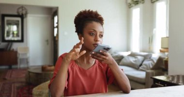 Ciddi, güzel, genç Afrikalı bir kadın akıllı telefonuna sesli mesaj bırakıyor, cep telefonunu ağzında tutuyor, konuşuyor, mutlu oluyor, gülümsüyor, konuşmalarını bitiriyor, daktilo ediyor, evde oturuyor.