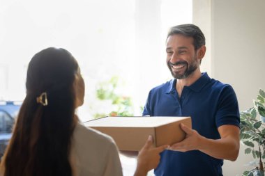 Orta yaşlı mutlu kurye kadın müşteriye lojistik karton kutu veriyor. Paketi eve teslim ediyor. Pozitif teslimatçı, nakliye servisi çalışanı işten zevk alıyor.