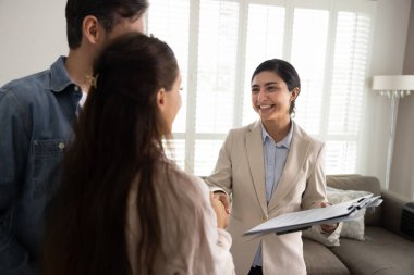 Mutlu Hintli genç bir emlakçı, kapalı bir yerde birkaç ev alıcısıyla görüşüyor, anlaşmayı imzaladıktan sonra el sıkışıyor, yasal evrakları tutuyor, gülümsüyor, satın aldığınız için tebrik ediyor.