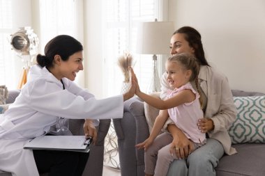 Neşeli genç Hintli doktor küçük beyaz hasta kıza beşlik çakıyor başarılı bir muayeneden sonra mutlu çocukla el çırpıyor anne ve kızını evinde ziyaret ediyor.