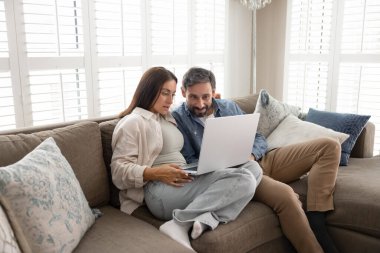 Genç, orta yaşlı çift kanepelerinde dizüstü bilgisayarlarıyla rahatlıyor, film izliyor, internetten video içeriği alıyor, e-alışveriş için online başvuru kullanıyor, rezervasyon yaptırıyor.