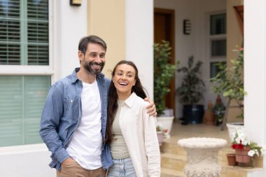 Mutlu Latin çift yeni evin bahçesinde duruyor, sarılıyorlar, uzağa bakıyorlar, gülümsüyorlar, gülüyorlar, ev sahipliğinin tadını çıkarıyorlar emlak alım satımları, emlak anlaşmaları, ipotek borçları.