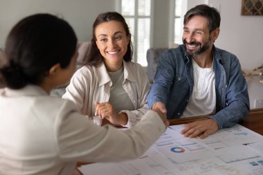 Konsültasyon için finansal danışmana teşekkür eden, masadaki kağıt analizlerinin üzerinden el sıkışan, kişisel yatırım planlayıcısına el sıkışan, gülümseyen, toplantıyı bitiren mutlu bir çift.