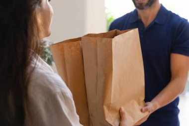 Erkek yemek siparişi getiren adam, kağıt paketler dolusu yiyecek veriyor, süpermarketten kadın alıcıya yemek veriyor. Müşteri kadın kuryeden poşet ve erzak alıyor. Kırpılmış atış