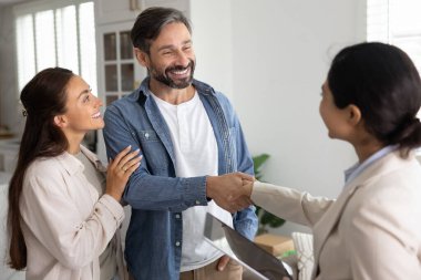 Birkaç pozitif memnun emlak alıcısı Hintli kadın emlakçıya el sıkışırken, yardım için mortgage komisyoncusuna teşekkür ederken, daire satın alırken, gülümserken, gülerken,