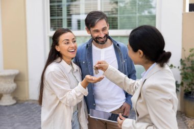 Neşeli ev alıcıları, emlakçı kadından anahtar alıyorlar, ilk konaklama yerini alıyorlar, yeni ev, emlakçıyla anlaşma yapıyorlar, gülümsüyorlar, gülüyorlar, bahçede duruyorlar.