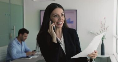 İtalyan iş kadını toplantı odasında duruyor, belgeyi incelerken profesyonel telefon görüşmeleri yapıyor, iş konularını tartışıyor, raporları analiz ediyor, sözleşme detaylarını telefonla anlatıyor.