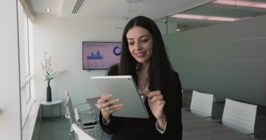 Modern konferans odasında tablet kullanan iş kadını, mali verileri gözden geçiriyor veya sunuma hazırlanıyor, dijital ekran arka planda grafik ve grafiklerle iş analizlerini gösteriyor