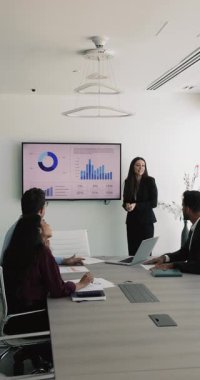 Takım elbiseli genç profesyonel iş kadını personel veya şirket müşterilerine sunum yapıyor, ekran görüntüsü ve bar grafiklerinin yanında duruyor, analitik veri açıklaması ve anahtar ölçümleri sağlıyor