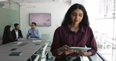 Güzel Hintli iş kadını toplantı odasında modern dijital tablet kullanarak duruyor, işle ilgili sorunları e-posta ile çözüyorlar, sohbet ediyorlar, müşteriye cevap veriyorlar, yeni platformu gözden geçiriyorlar, online sunum hazırlıyorlar.