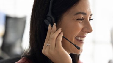 Neşeli çağrı merkezi operatörü kablosuz kulaklığa ve mikrofona dokunuyor, müşteriyle sohbet ediyor, gülümsüyor, gülüyor, telefon desteği veriyor, yardım, yardım. Çalışan yüzünü kapat, afiş resmi