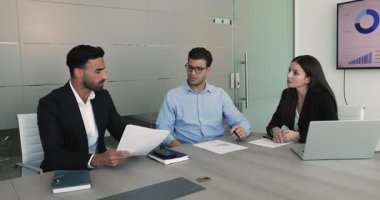 Modern toplantı odasındaki konferans masasında oturan çok uluslu takım, anlaşma ayrıntılarını, sözleşme şartlarını gözden geçirir, takım çalışmasına ilişkin müzakereler için yasal belgeleri hazırlar.